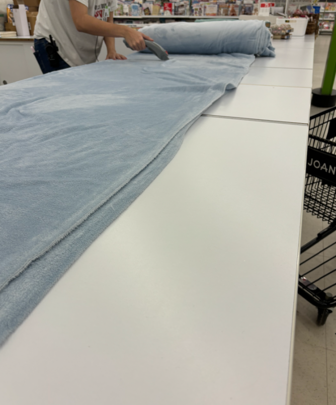 A person cutting light blue fleece fabric at a fabric store